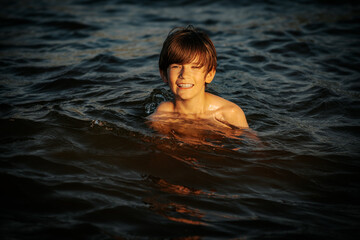 A boy swimming in the ocean, smiling and flashing a peace sign with his fingers. The image captures a joyful and carefree moment during a summer day at the beach