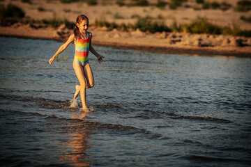 A girl in a colorful swimsuit walking through the ocean waves, enjoying the summer day. The image captures a serene and playful moment by the sea