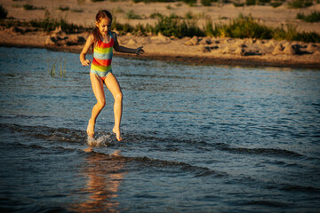 Naklejka premium A girl in a colorful swimsuit walking through the ocean waves, enjoying the summer day. The image captures a serene and playful moment by the sea