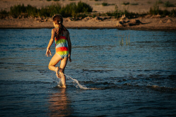 A girl in a colorful swimsuit playing energetically in the ocean waves, capturing a moment of joy and movement by the sea. The image emphasizes the fun and excitement of a summer day at the beach