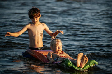 Two boys having fun on an inflatable raft in the water at the beach during sunset. The image...