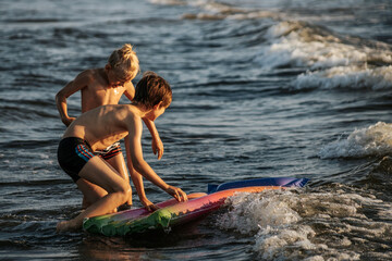Two boys having fun on an inflatable raft in the water at the beach during sunset. The image...