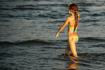 A girl in a colorful swimsuit playing energetically in the ocean waves, capturing a moment of joy and movement by the sea. The image emphasizes the fun and excitement of a summer day at the beach