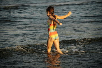 A girl in a colorful swimsuit playing energetically in the ocean waves, capturing a moment of joy and movement by the sea. The image emphasizes the fun and excitement of a summer day at the beach