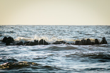 Waves crashing on a cluster of coastal rocks, with the sea stretching out to the horizon. The image captures the power and beauty of the ocean in a serene and natural setting.