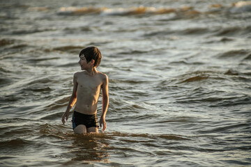Fototapeta premium A boy energetically splashing in the ocean waves, creating a burst of water droplets around him. The image captures the fun and excitement of a day at the beach, with the boy enjoying the summer sun