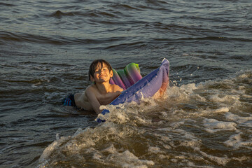 A boy riding an inflatable raft in the waves at the beach, capturing a moment of fun and adventure in the water. The image shows his determination and enjoyment as he navigates the waves.