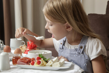 Cute little girl having breakfast, cereals with yogurt, tasty and healthy choice between various dishes served on the table