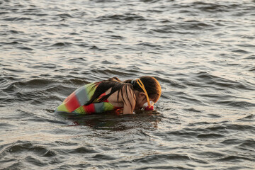 A girl in a colorful swimsuit and pink goggles playfully splashing in the waves at the beach during...