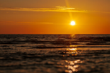 A serene sunset over the ocean with a glowing orange sky reflecting on the water. The image captures the peaceful beauty of the sea at dusk, creating a tranquil and picturesque scene