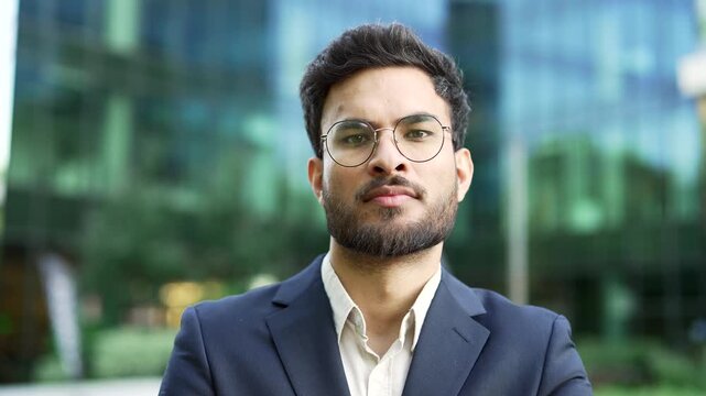 Portrait of a confident businessman in suit standing on the street near a business office building. Serious male entrepreneur in glasses posing looking at camera. Head shot of the manager. Close up 