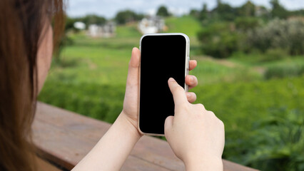 Close up image of a business woman's hands holding and using smartphone on wooden table and natural background with black blank screen for display your graphic.