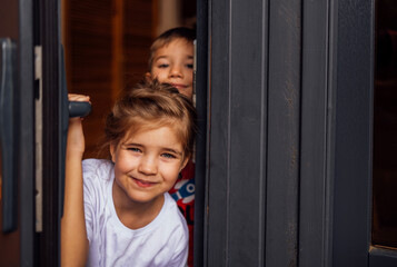 Close-up of cute children peeking out of the doorway. Little brother and sister open the front...
