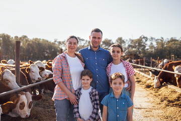 A young happy family of farmers in a cowshed. A smiling woman, a man and three kids in casual...