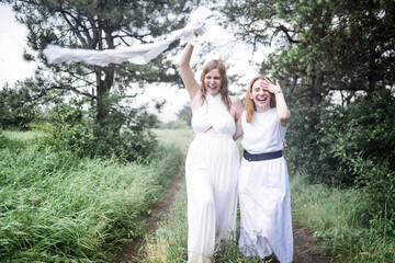 Naklejka premium Two charming girls in white dresses are running in the summer rain