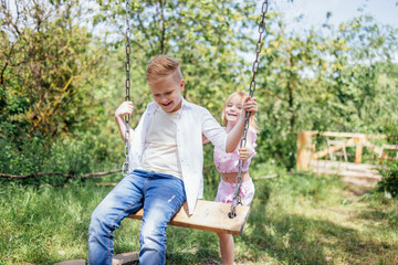 Pretty little girl in summer is rocking her brother on swing.