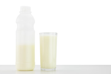 Glass of fresh milk and bottle of milk on white table on white background