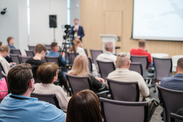 Obraz premium Attendees listening to presentation during a business conference in an auditorium. Speaker and camera recording in background