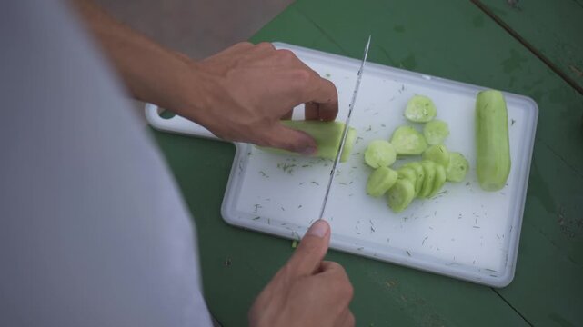 A professional chef demonstrates their culinary skills by precisely cutting a fresh cucumber on a wooden board and crafting a nutritious salad with organic ingredients using healthy cooking methods