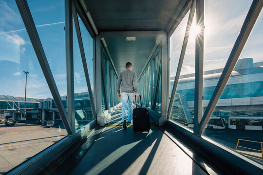 Travel by airplane. Rear view of man with hand baggage walking in passenger boarding bridge at airport on sunny day..
