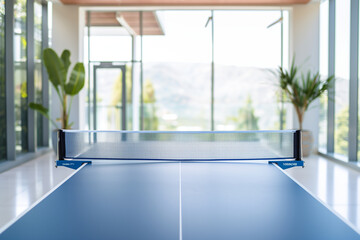 Fototapeta premium Table tennis game setup with a blue ping pong table, net, and ball in a modern indoor play room. Perfect for showcasing a professional championship competition or recreational hobb