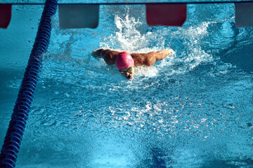 Competitive swimmer, wearing pink swim cap and goggles, powers through water with butterfly stroke,...