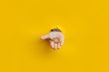 A golden bracelet in a child's hand protrudes through a torn hole in yellow paper. Concept of precious jewelry.