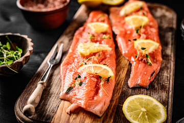 Fresh trout salmon filet with rosemary and lemons on wooden board ready served with knife. Omega orange fish with citrus fruit for healthy nutrition