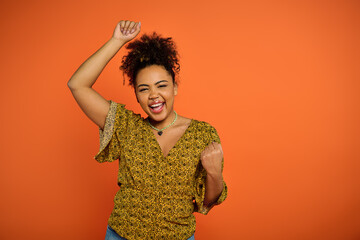 Beautiful African American woman in stylish attire joyfully raises her arms in the air against a...