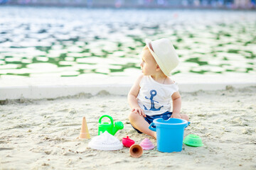 a baby boy of six months plays in the sand with toys on the embankment by the water of the sea, the concept of recreation and travel