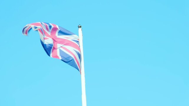 Union Jack flag soars against backdrop clear blue sky, United Kingdom's heritage, resilience, and unwavering spirit