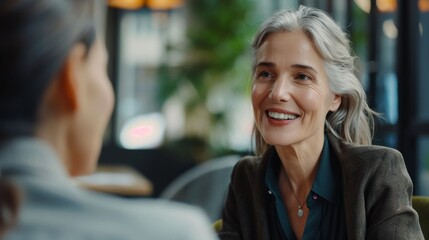 A happy senior woman listens intently to her friend, enjoying a conversation over coffee in a cozy cafe.  The image symbolizes friendship, connection, communication, and active listening.