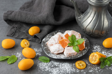 Sweet kumquat oriental delight lokum closeup and fresh raw whole and sliced fruits with mint leaves on retro metallic plate on dark stone table background.