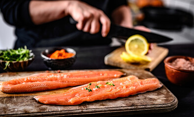 Fresh trout salmon filet with herbs and salt on wooden board and chief hands cutting lemons on blurred background. Omega orange fish with rosemary for healthy nutrition