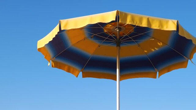 Beach umbrella in blue and yellow colors against a clear sky background with empty copy space