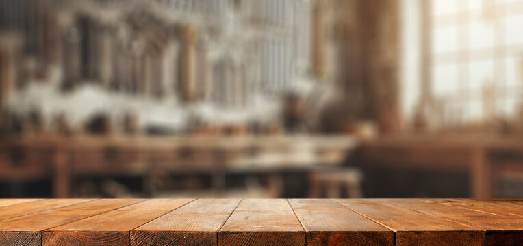 Empty wooden work table with space for tools and products. Blurred background of craft workshop and wall with tools.
