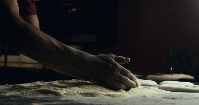 Super slow motion of professional artisan baker chef kneads dough with flour while making homemade bread, pasta or pizza on rustic wooden table in traditional bakery kitchen.