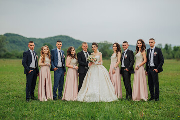 A group of people are posing for a photo in a field. The bride and groom are in the center of the...