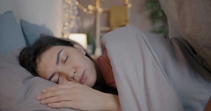 Young woman sleeping in bed while loving husband covering with blanket and kissing expressing love. Family lifestyle and relationship concept.