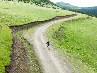 Aerial view of woman riding mountain bike on flowering grassland mountain trail