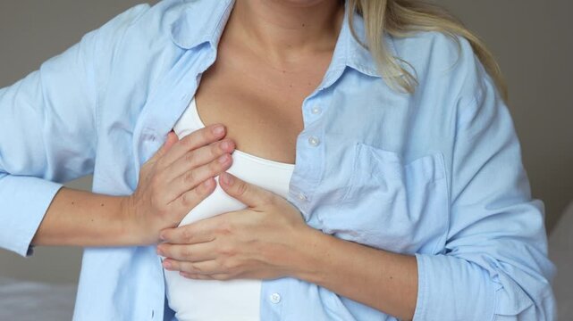 The young blonde woman feeling discomfort in her breast suffering from a pain during period. Cropped shot of a girl checking breast groping for seals on a grey background. Self-examination