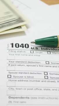 100 dollar bills on 1040 tax form. Green pen on table in office. U.S. individual income tax return. Tax payment concept. Filing taxes document. Count the money
