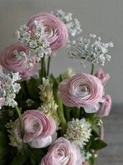 Beautiful tender pink ranunculus flowers, white ornithogalum and hyacinths flowers in a floral composition, close up vertical view on the grey wall background 