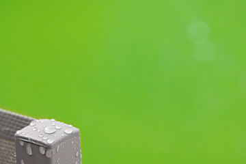 A minimalistic image of the corner of a grey garden chair with raindrops on set against the green of the grassy garden area, much space for text