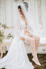 A woman in a white gown sits on a bench with her legs crossed. She is wearing a veil and a white wedding dress