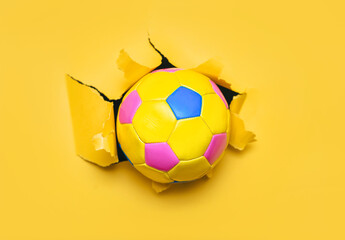 Colorful children's soccer ball breaks through yellow paper wall. Concept of early age sports,...