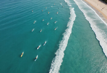 An aerial view of a group of surfers riding waves on a pristine beach with turquoise water.