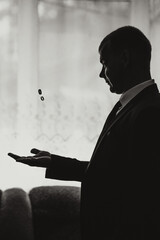 A man in a suit holding a ring in his hand. The man is wearing a tie and is standing in front of a window