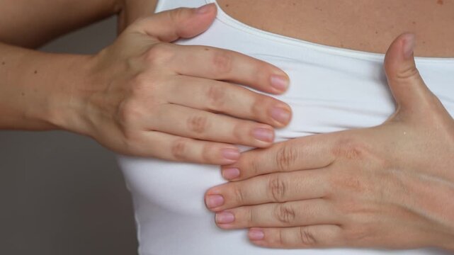 The girl suffering from a pain in her breast during menstruation. Cropped shot of young woman checking breast feeling discomfort on a grey background. Self-examination. Close up