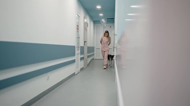 Side view of a confident girl in a pink uniform escorting a black dog to its owner in a veterinary clinic. Girl veterinarian with a black dog in the clinic